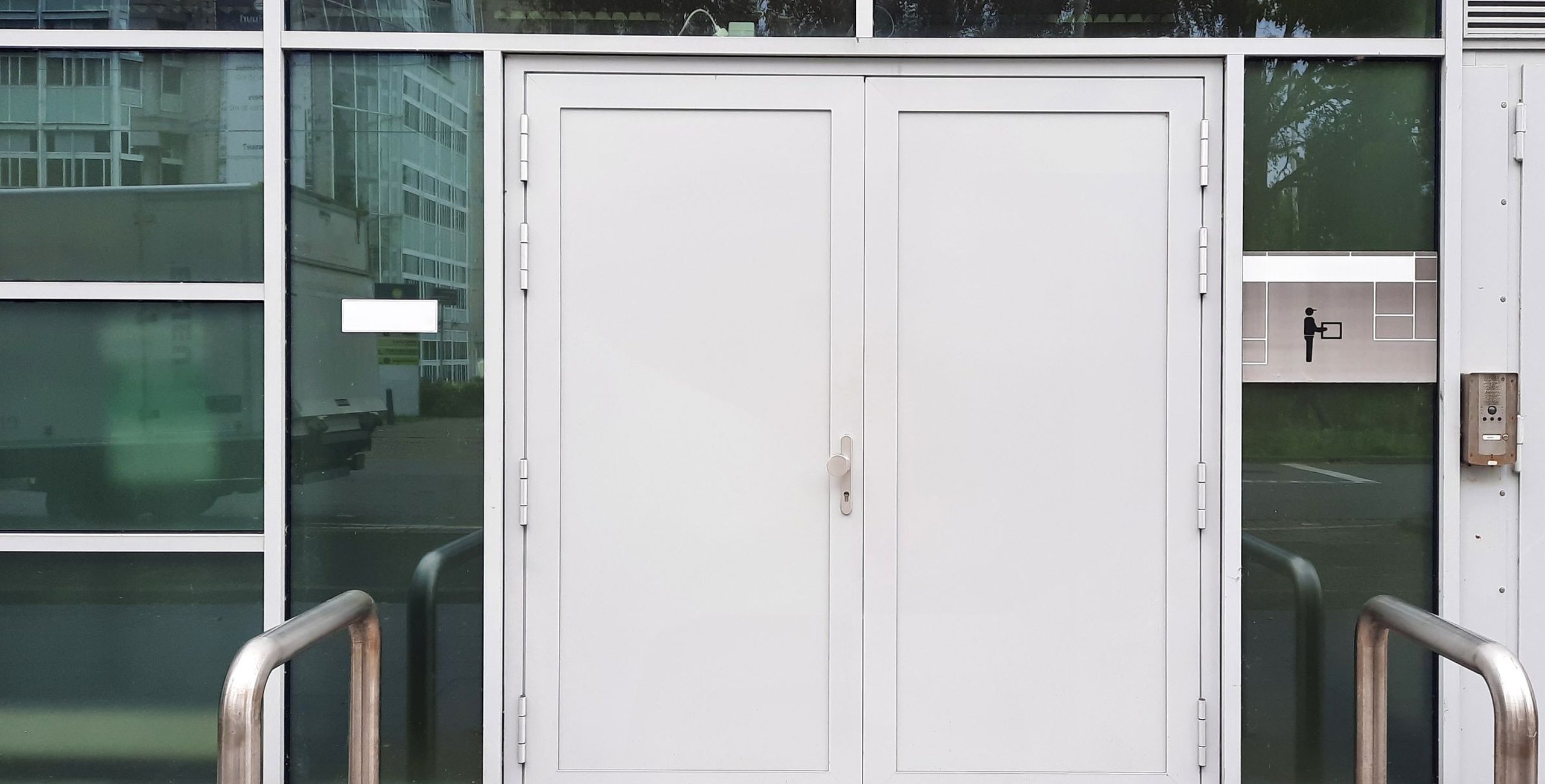 White aluminum double entrance doors in a glass storefront, with bollards at the curb